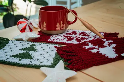 Holiday Crochet Mug Rugs with tree and deer designs under a red mug on a wooden table