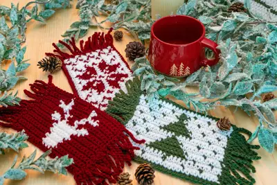 Holiday Crochet Mug Rugs in red and white with deer and trees beside a red mug