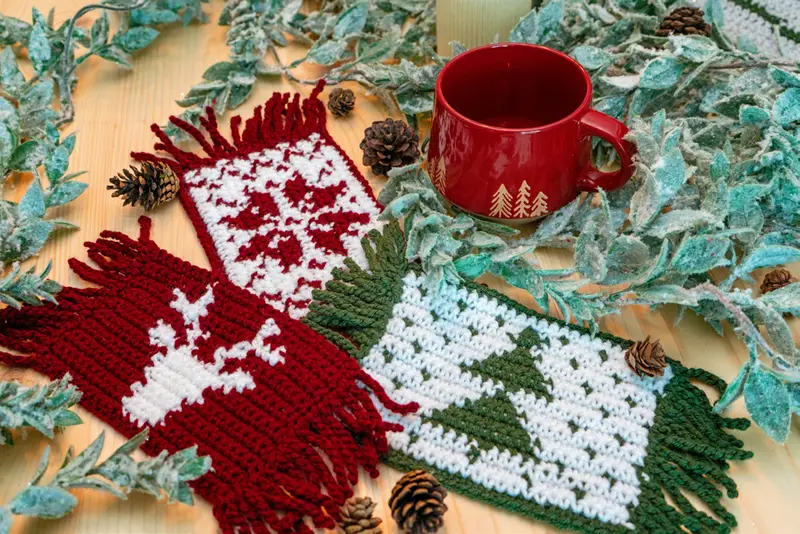 Holiday Crochet Mug Rugs in red and white with deer and trees beside a red mug