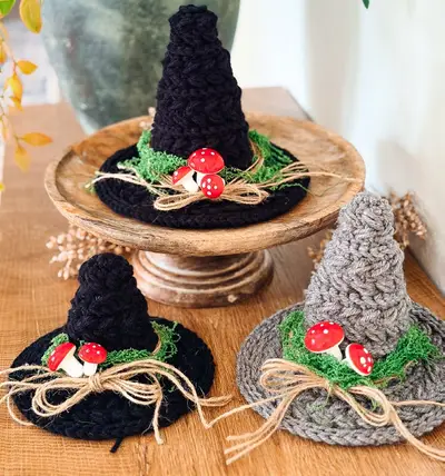 Black and gray crochet witch hats with mushroom and moss trim on wooden stands