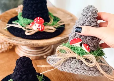 Gray and black crochet witch hats with red mushroom accents on a wooden stand