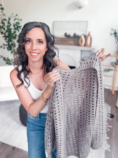 Woman holding up the gray Hummingbird Cardi to show the open lace stitch