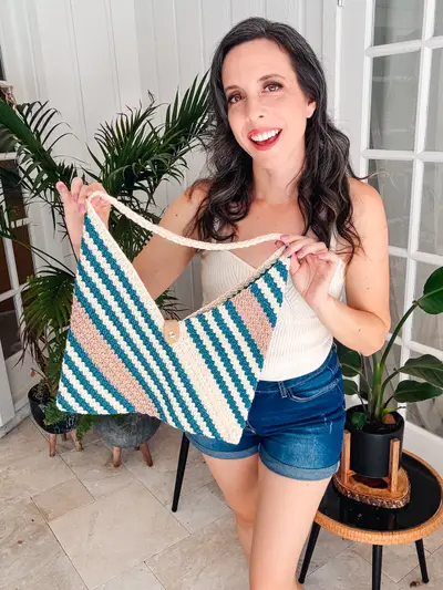 Woman holding the striped Just a Rectangle Crochet Bag with denim shorts