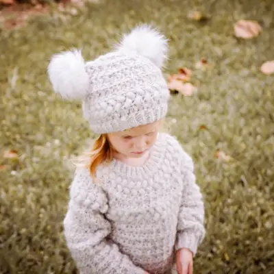 Little girl in an oatmeal Macchiato Crochet Beanie with two white pom pom ears
