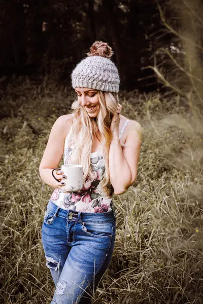 Woman wearing an oatmeal Macchiato Crochet Beanie in a grassy field holding a mug