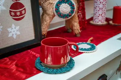 Teal Macchiato Crochet Coaster under a red mug on a holiday table runner