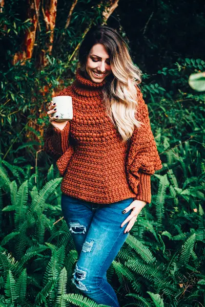Woman in the rust Macchiato Crochet Poncho holding a mug among ferns