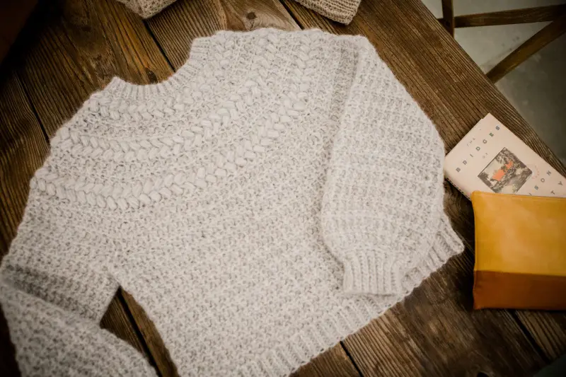 Child size Macchiato Crochet Sweater in oatmeal laid flat on wood