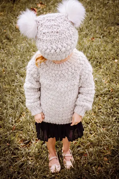Little girl in an oatmeal Macchiato Crochet Sweater and matching pom pom beanie