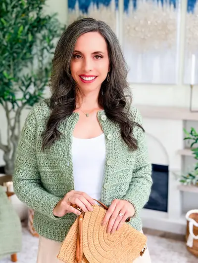 Sage Petal Loop Cardigan worn over a white top, holding a straw clutch