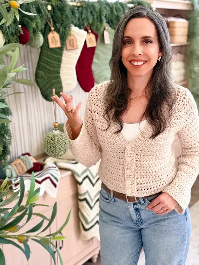 Woman holding a sage Petal Loop Stitch Ornament in a holiday room