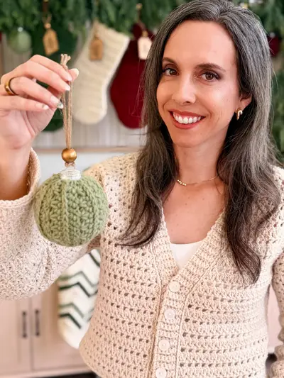 Smiling woman holding a sage Petal Loop Stitch Ornament by its ribbon