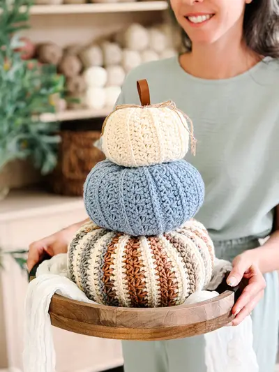 Woman holding a stack of Petal Loop Stitch Pumpkins in cream, blue and striped