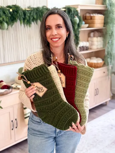 Woman holding four Petal Loop Stitch Stockings in green, cream, red and sage