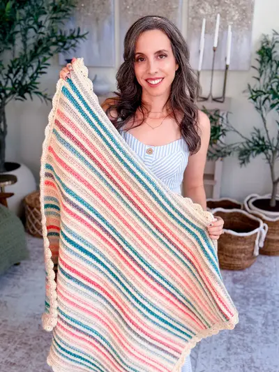 Woman holding up the Petal Loop Stitch Striped Blanket in pink, teal and cream