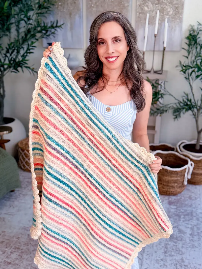 Woman holding up the Petal Loop Stitch Striped Blanket in pink, teal and cream