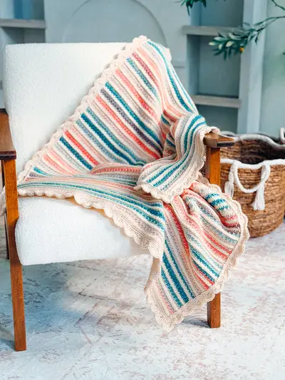 Petal Loop Stitch Striped Blanket in teal, pink and cream on a white armchair