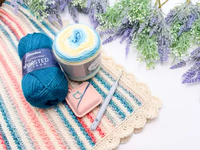 Striped blanket with skeins of teal and ombre yarn and a crochet hook