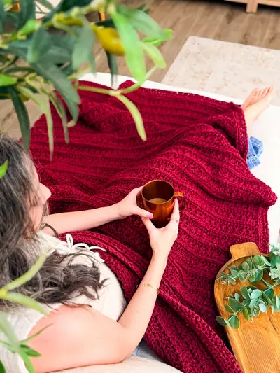 Woman relaxing under a red Petal Loop Stitch Textured Blanket with a mug
