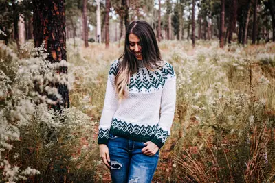 Woman wearing the white and green Pine Fair Isle Crochet Sweater in a forest