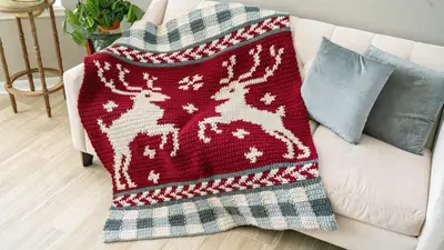 Red Prancing All the Way Deer Crochet Blanket on a white sofa with gray pillows