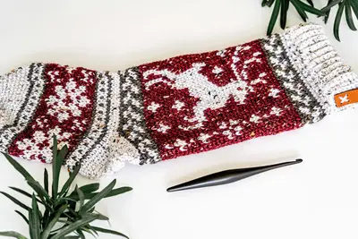 Prancing Deer Holiday Stocking laid sideways with pine and a crochet hook