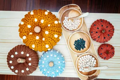 Overhead view of beaded crochet pumpkins in four colors with wooden bowls of beads