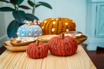 Orange beaded crochet pumpkins on a wooden table with blue and mustard pumpkins