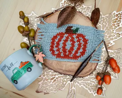 Fringed crochet pumpkin mug rug on a wood slice next to a Welcome Fall mug