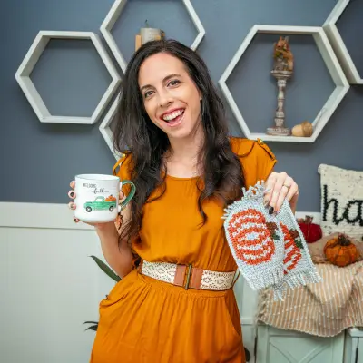 Smiling woman in mustard holding a fall mug and two pumpkin mug rugs