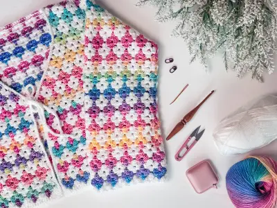 Rainbow Hues Crochet Cardigan laid flat with a skein of rainbow yarn