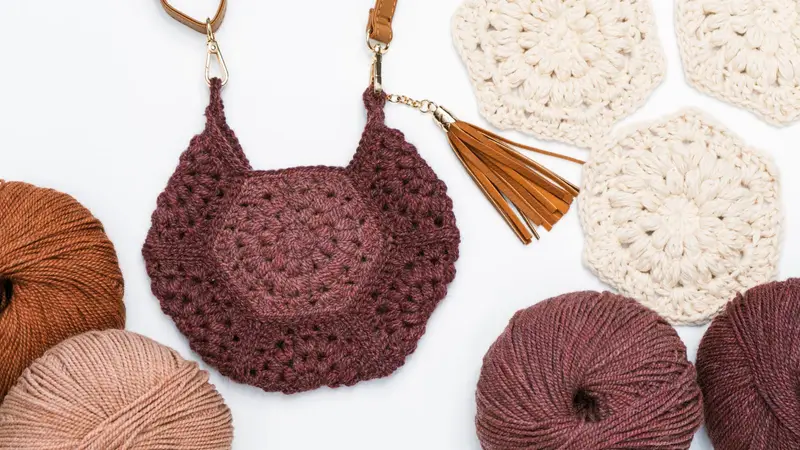 Brown Seven Hexi Granny Bag with a leather tassel beside skeins of yarn