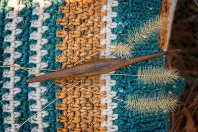 Close up of moss stitch stripes in teal, cream and gold with a wooden hook