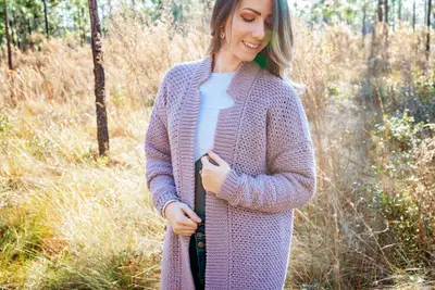 Smiling woman in a solid mauve Shortbread Crochet Duster in a sunny field