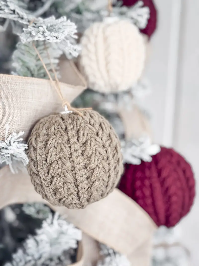 Snowy Wheat Ornament in taupe hanging on a flocked tree with red and cream ornaments