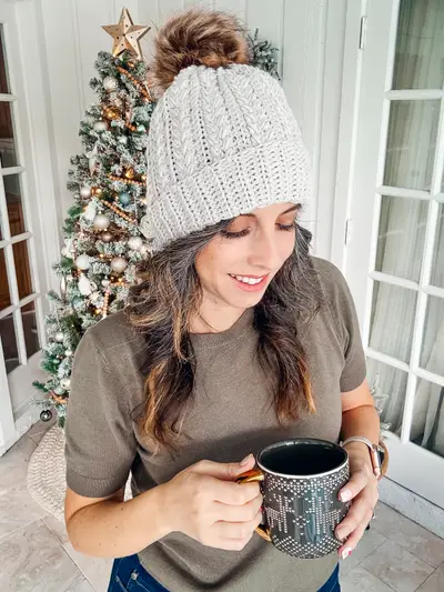 Woman in a light gray Snowy Wheat Stitch Crochet Hat holding a mug by a Christmas tree