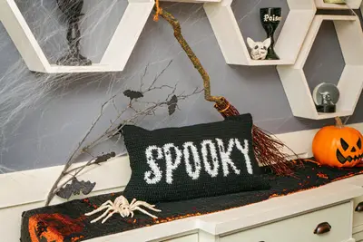 Spooky Crochet Pillow Cover on a dresser with a broom, bats and jack o'lantern