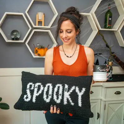 Woman in an orange top holding the Spooky Crochet Pillow Cover