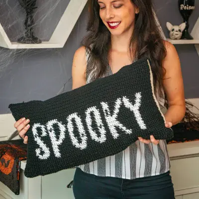 Woman holding up the black Spooky Crochet Pillow Cover with white letters