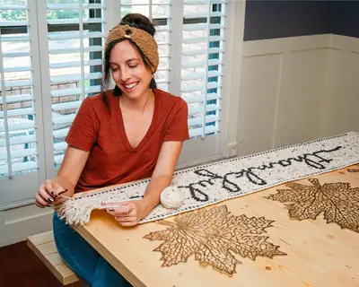 Smiling woman adding fringe to the Thankful Crochet Table Runner at a table