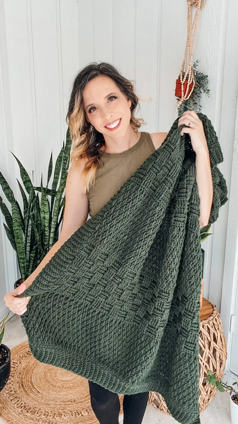 Woman holding up the forest green Totally Textured Crochet Blanket