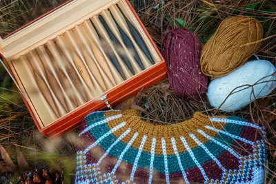 Traveler Fair Isle yoke laid flat with skeins of yarn and a box of crochet hooks