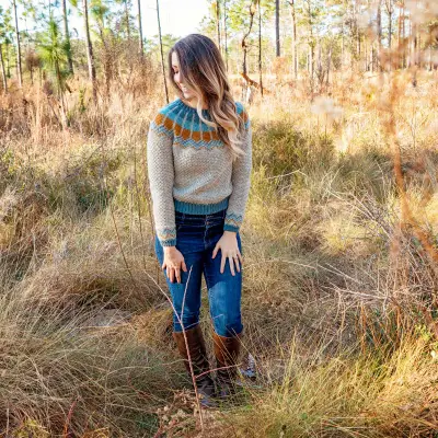 Woman wearing the gray Traveler Fair Isle Crochet Sweater in a pine forest
