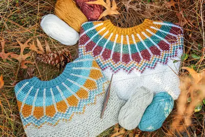 Two Traveler Fair Isle yokes laid flat with skeins of yarn and pine cones