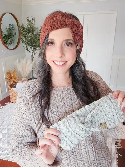Woman wearing a rust Twisted Wheat Ear Warmer and holding a gray one