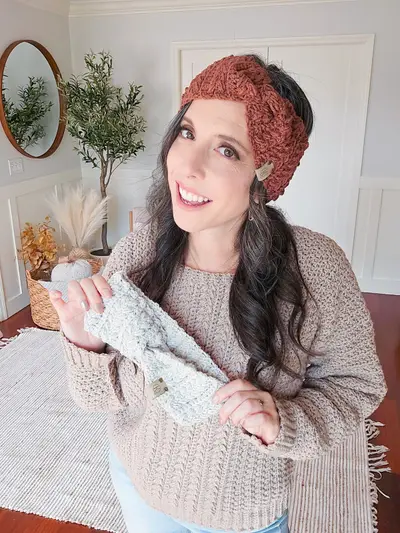 Smiling woman in a rust Twisted Wheat Ear Warmer holding a pale blue one