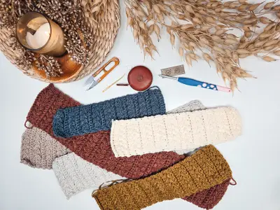Twisted Wheat Ear Warmers laid flat before twisting, with scissors and a candle