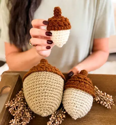 Hand holding a small Wheat Stitch Acorn above larger acorns on a tray