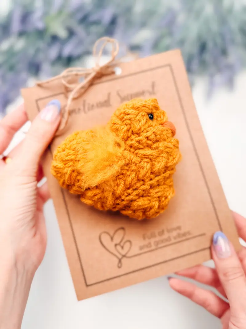 Hand holding a golden yellow Wheat Stitch Chick on a kraft gift card