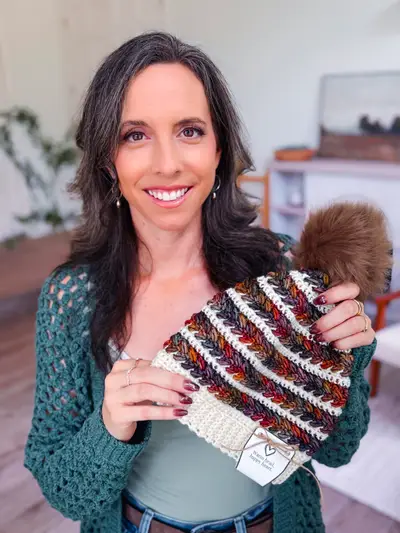 Smiling woman holding a striped Wheat Stitch Crochet Beanie
